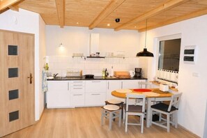 Kompakti keittiö, jossa on valkoiset kaapit, puinen ruokapöytä ja riippuvalaisin.