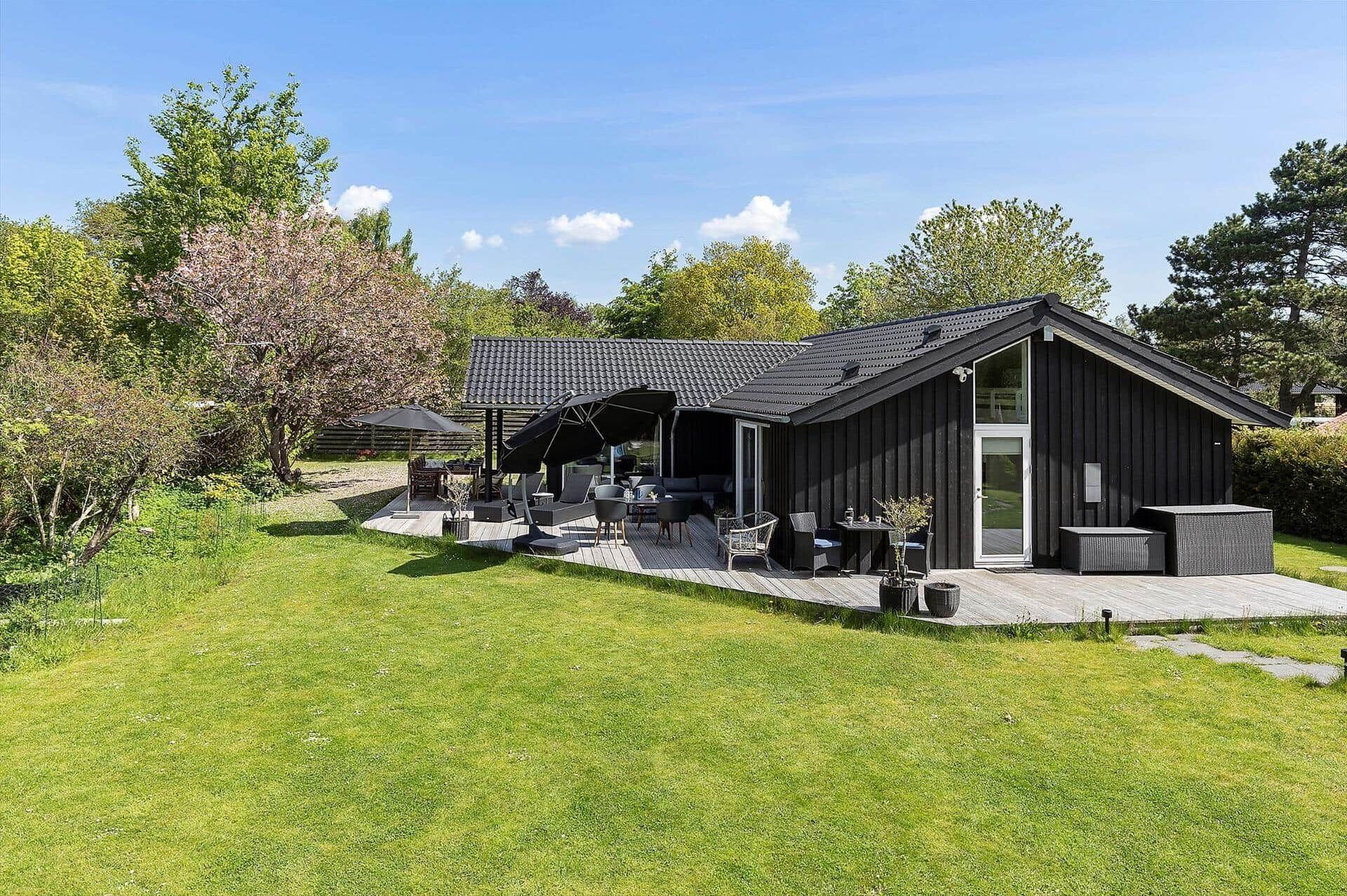 Een modern buitenpatio met zitplaatsen en een overdekt gedeelte, omringd door een verzorgd gazon en bomen.
