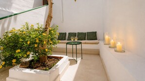 Ein raumheller Raum mit einem kleinen Tisch, zwei grünen Kissen und einer Topfpflanze mit gelben Blüten.