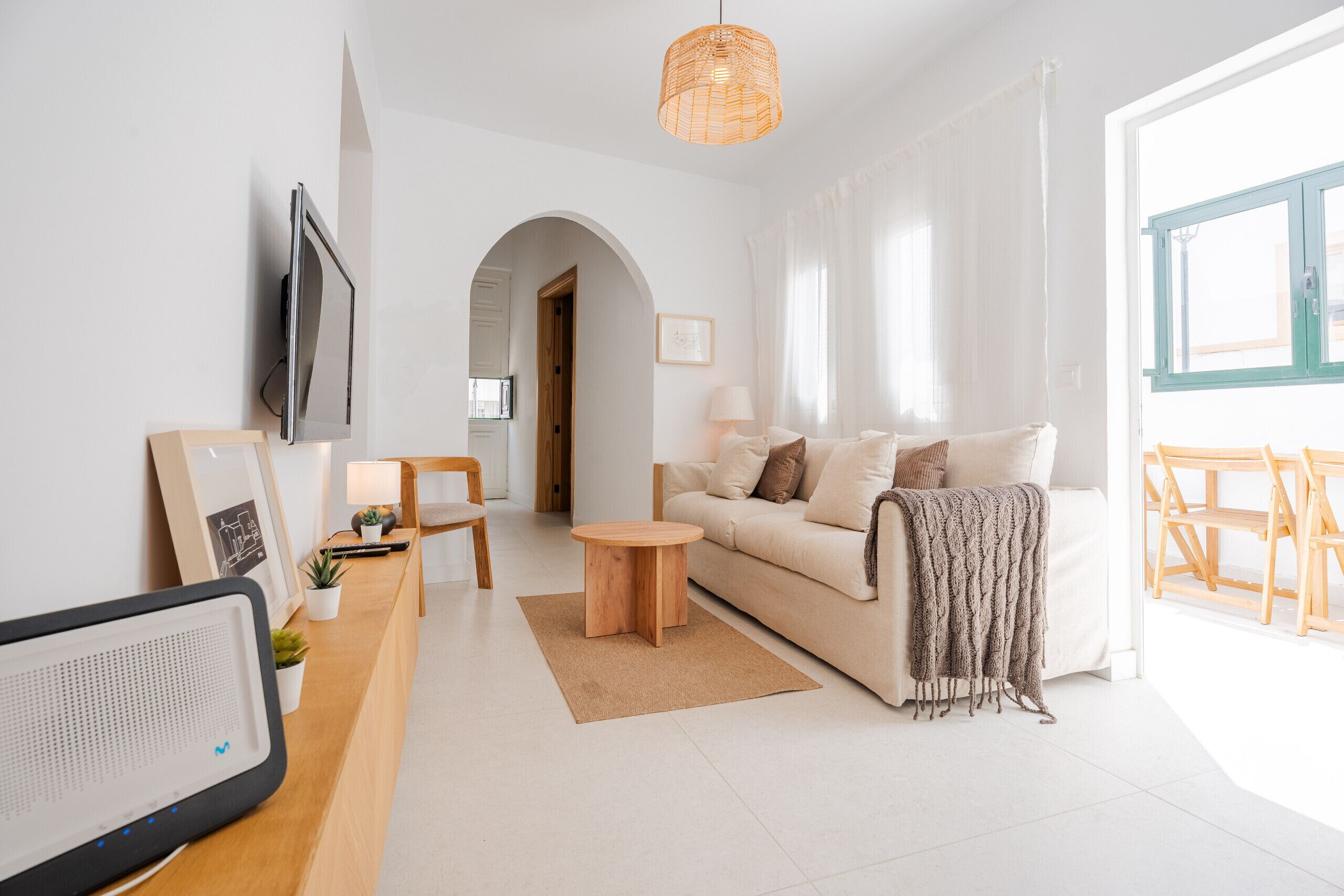 En moderne stue med sofa, sofabord, tv og udsigt til det fri.