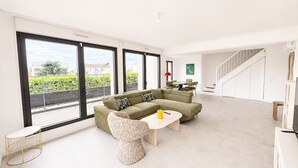 A spacious living area with a large sofa, a round coffee table, and a view of greenery through large windows. - Appartement 2 chambres avec terrasse a Courbevoie (Courbevoie)