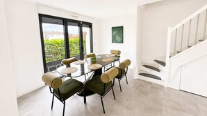 A dining area with a round table and six chairs, a staircase, and a view of greenery outside. - Appartement 2 chambres avec terrasse a Courbevoie (Courbevoie)