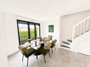 Spiseplads med et rundt bord og seks stole, en trappe og udsigt til grønne omgivelser.