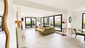 A spacious living room with a sofa, a coffee table, and a dining area with a table and chairs. Large windows provide views of the city. - Appartement 2 chambres avec terrasse a Courbevoie (Courbevoie)
