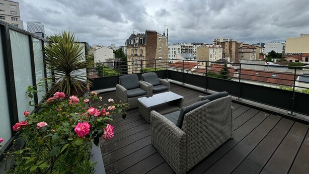A rooftop terrace with wicker furniture, a table, and pink flowers. - Appartement 2 chambres avec terrasse a Courbevoie (Courbevoie)
