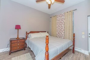 Une chambre à coucher avec un lit en bois, une table de chevet, une lampe, un ventilateur de plafond et un rideau à motifs.