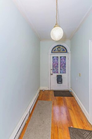 Un couloir doté d’un plancher en bois, d’une porte blanche avec une plaque numérotée et d’un luminaire suspendu.