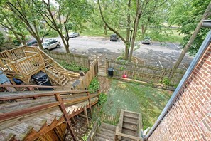 Un jardin avec un escalier en bois, un mur de briques et une vue sur un parking rempli de voitures.