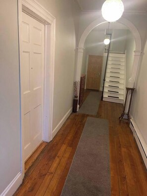 Un couloir doté d’un plancher en bois, d’une porte blanche et d’un escalier avec une rampe blanche.