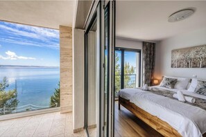 A bedroom with a large bed, a painting on the wall, and a view of the sea through a sliding door. - Villa Aurora Paklenica (Starigrad)