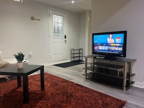 Ein Wohnzimmer mit Fernseher, Couchtisch, Topfpflanze, einer TĂŒr mit SchlĂŒssel und einem schwarzen MetallstĂ€nder.
