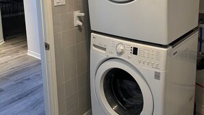 A stacked washer and dryer unit in a room with tiled walls and a wooden floor. - Entire Private Suite! Free Parking! Comfortable Stay! Excellent Location! (Pickering)