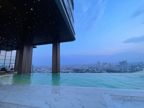 An infinity pool with a city view, a modern building structure, and a clear sky. - City View Room At Vue Aston by VS (Phnom Penh-ភ្នំពេញ)
