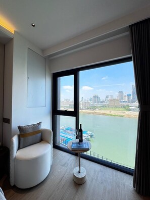 A modern hotel room with a large window offering a city view, a round table with a bottle, and a white armchair. - City View Room At Vue Aston by VS (Phnom Penh-ភ្នំពេញ)