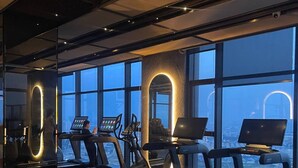 Ein Fitnessstudio mit Laufbändern, Ergometer und einem großen Fenster mit Blick auf die Stadt.
