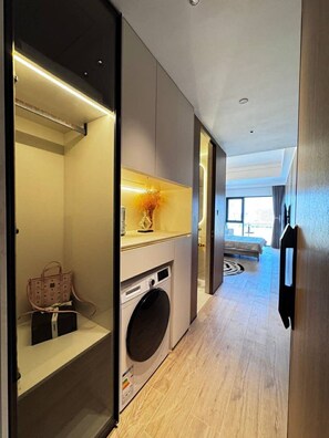 A modern hotel room with a washing machine, a bed, and a view of the city. - City View Room At Vue Aston by VS (Phnom Penh-ភ្នំពេញ)