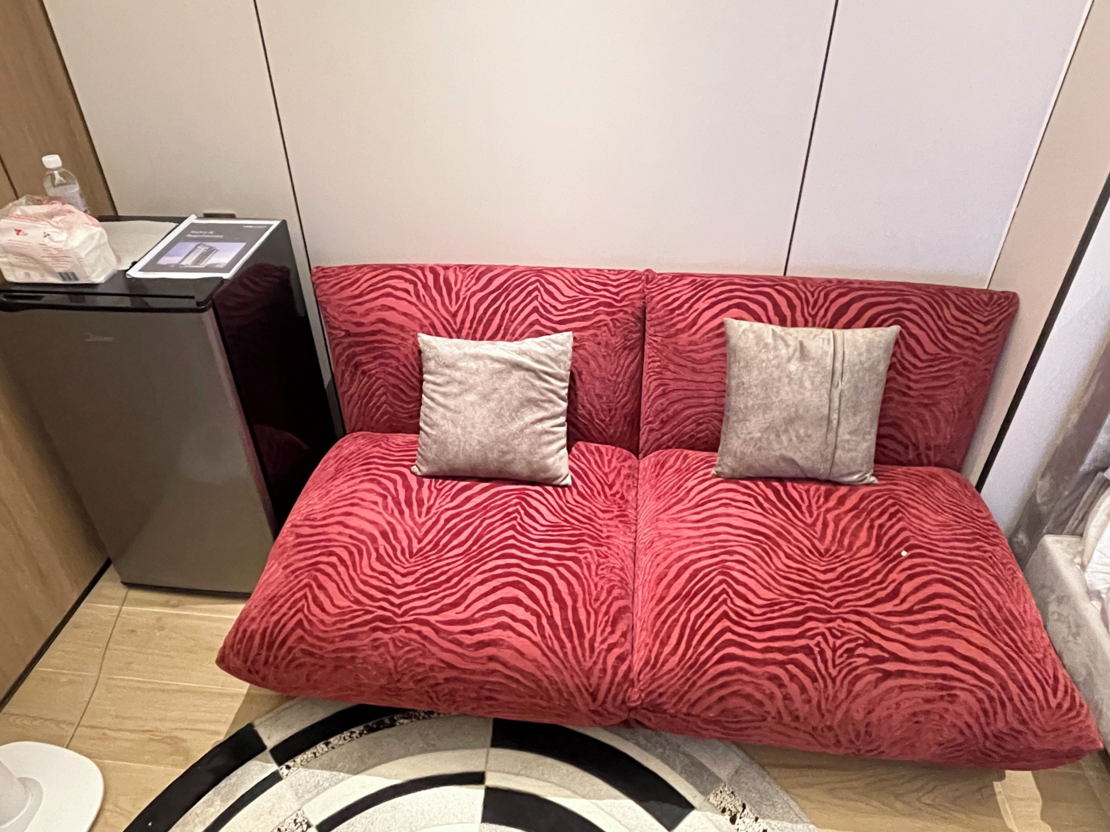 Un canapé rouge à motifs zébrés, agrémenté de deux coussins, un petit réfrigérateur et un sol carrelé.