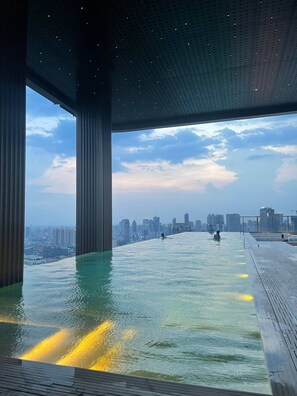 A rooftop infinity pool with a city skyline view, large pillars, and a wooden deck. - City View Room At Vue Aston by VS (Phnom Penh-ភ្នំពេញ)