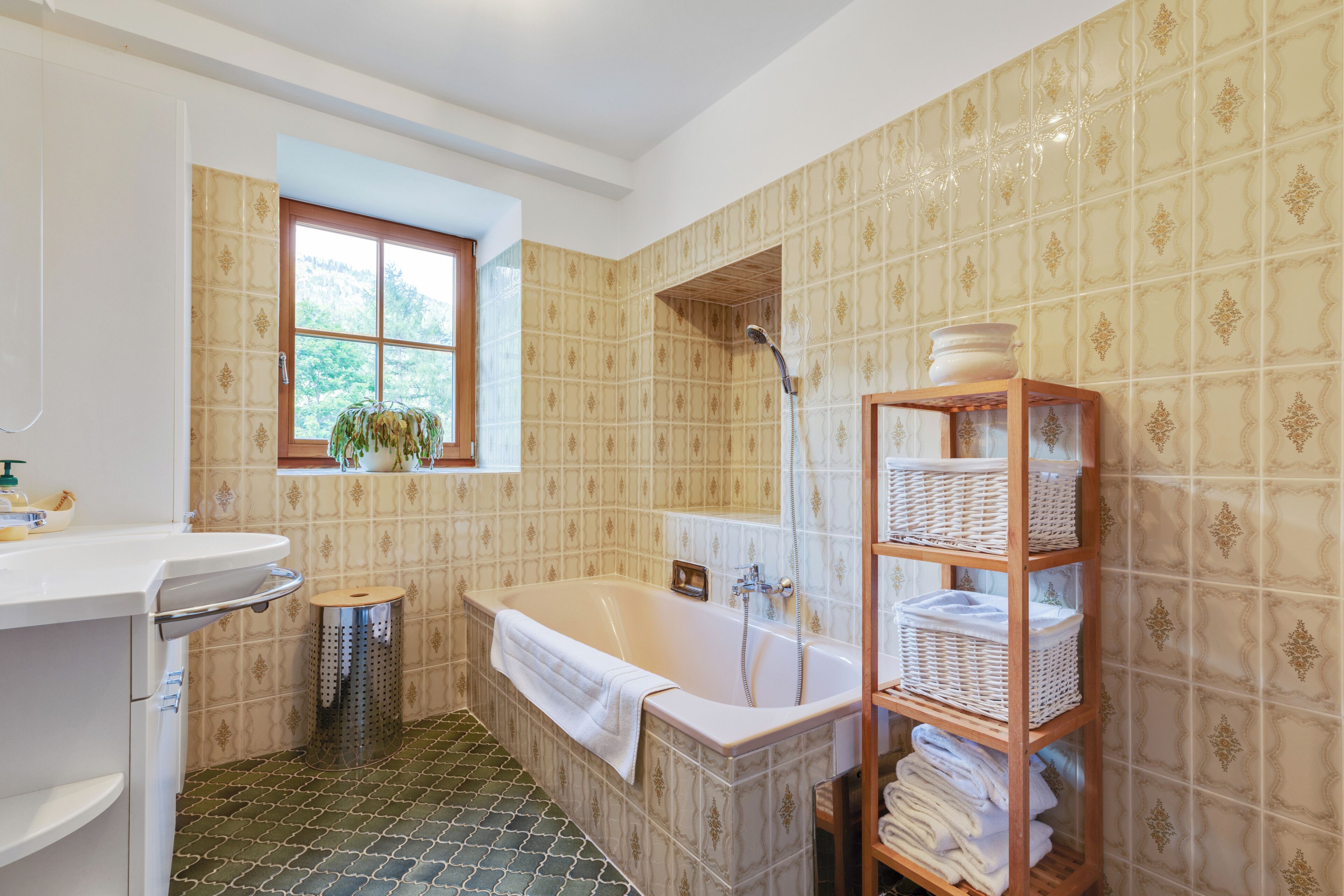 A bathroom with a bathtub, a window, a shelf with baskets, and a trash bin.