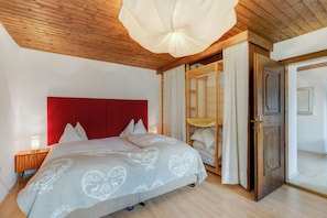A bedroom with a wooden ceiling, a red headboard, a bed with a patterned bedspread, a nightstand with a lamp, and a wardrobe with a mirror. - Ferienhaus Auwiese - Family Retreat (Lend)