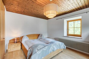 A bedroom with a wooden bed, a nightstand, a window with a view, and a ceiling fan. - Ferienhaus Auwiese - Family Retreat (Lend)