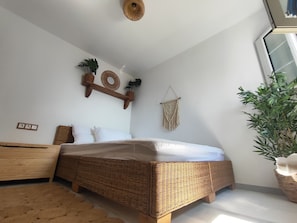 Une chambre avec un lit en osier, une décoration murale en macramé et une plante en pot.