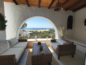 A covered outdoor seating area with wicker furniture and a view of the beach.