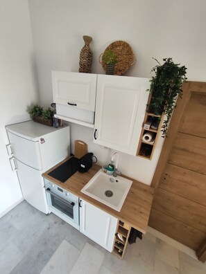 A compact kitchen with white cabinetry, a wooden countertop, a sink, a stove, and a small refrigerator. - Irini's Home Sea View Naxos Dream by ΜΡS (Pirgaki)