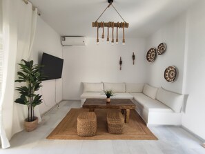 A living room with a sofa, a wooden coffee table, a hanging light fixture, a potted plant, and wall decorations.