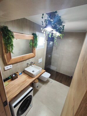A modern bathroom with a wooden vanity, a built-in sink, a mirror, a shower, and a washing machine. - Irini's Home Sea View Naxos Dream by ΜΡS (Pirgaki)