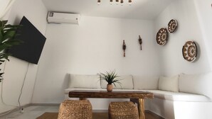 Una sala de estar moderna con un sofá blanco, una mesa de centro de madera, pufs tejidos, una lámpara colgante, adornos en la pared y un equipo de aire acondicionado.