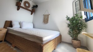 Una habitación con una cama de mimbre, un tapiz de macramé y una planta en maceta.