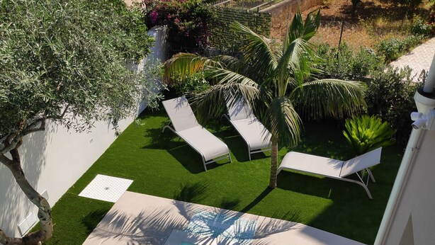 A swimming pool with a tiled deck, two lounge chairs, and a small garden area with a palm tree. - Apartment in villa with veranda and private pool (Castellammare del Golfo)