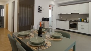 A modern kitchen with white cabinets, a dining table set for four, and a wine bottle on the table. - Apartment in villa with veranda and private pool (Castellammare del Golfo)