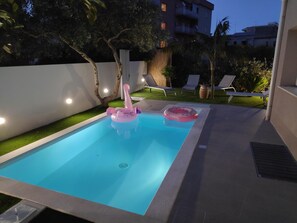Ein Swimmingpool mit einem rosa Flamingo-Schwimmpunkt und einem Donut-Schwimmpunkt, umgeben von einer kleinen Rasenfläche und Liegestühlen.