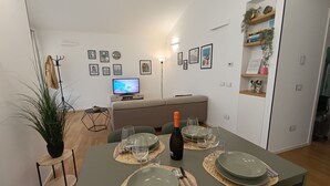A dining area with a table set for four, a television in the background, and a sofa. - Apartment in villa with veranda and private pool (Castellammare del Golfo)