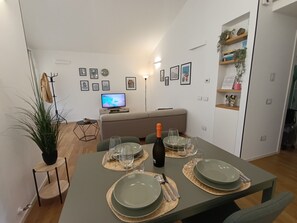 Ein Essbereich mit einem Tisch für vier Personen, einem Fernseher im Hintergrund und einer Couch.