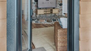 A doorway leading to a living area with a stone wall, a television, and a wicker chair. - Arla’s Pond Cottage - Scandinavian-Inspired Luxury in the Heart of Crosslake, MN (Crosslake)