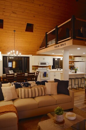 A spacious living area with a sofa, a dining table, and a kitchen in the background. - Arla’s Pond Cottage - Scandinavian-Inspired Luxury in the Heart of Crosslake, MN (Crosslake)