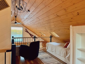 Ein Schlafzimmer im Spitzboden mit schrägen Wänden, einem Bett, einem Sessel und Blick ins Freie.