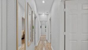 Un couloir aux murs blancs, doté d’un plancher en bois et d’une porte au fond.