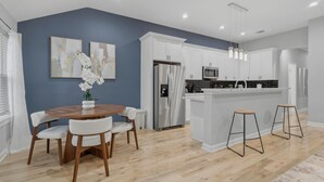 Une cuisine moderne avec des meubles blancs, des appareils en acier inoxydable et une table à manger en bois, assortie de chaises blanches.