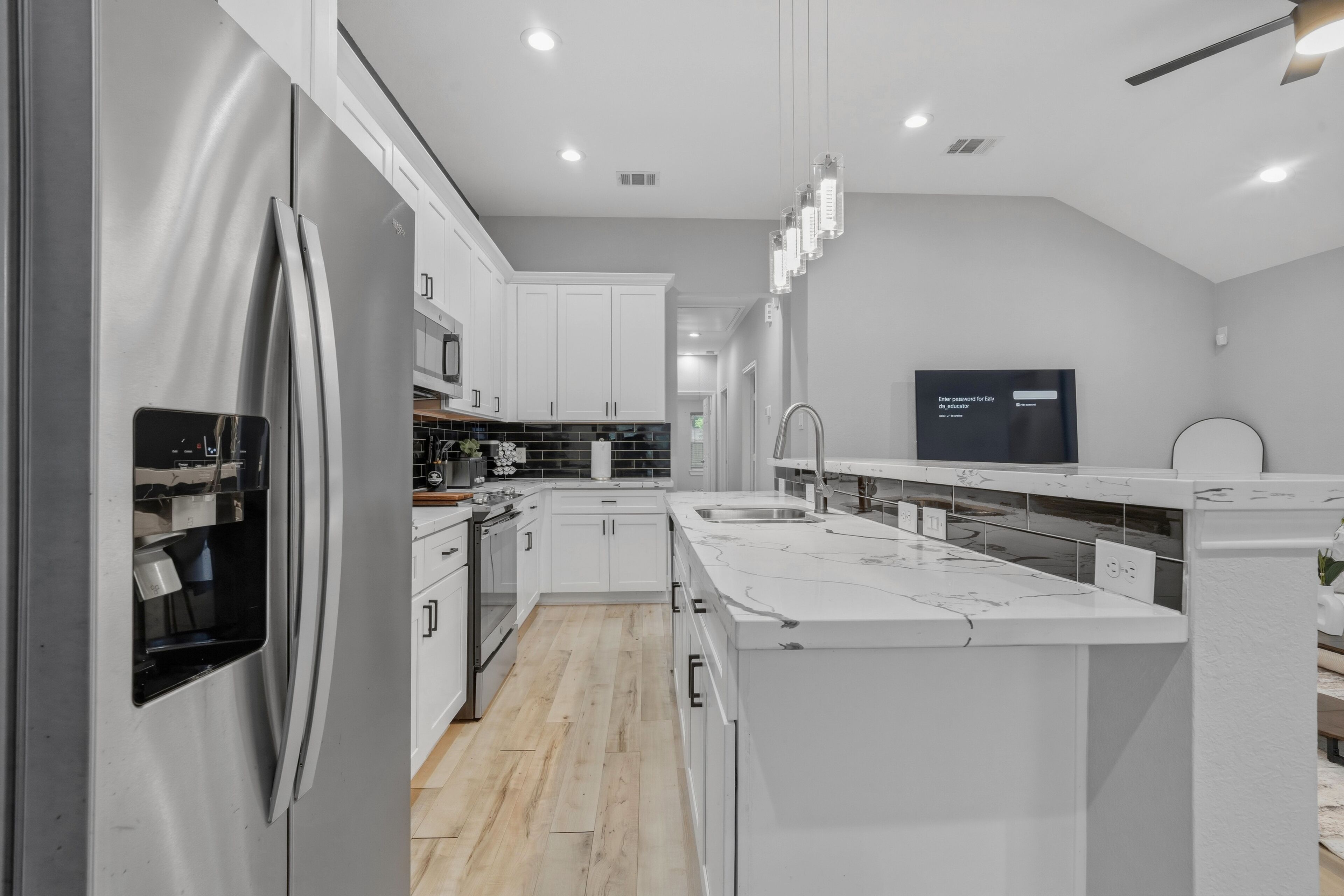 A modern kitchen with white cabinetry, a stainless steel refrigerator, a built-in oven, and a large island with a sink.