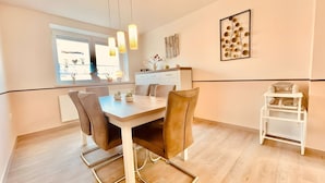 Ein moderner Essbereich mit Holztisch, Ledersesseln, Pendelleuchten und Blick ins Freie.