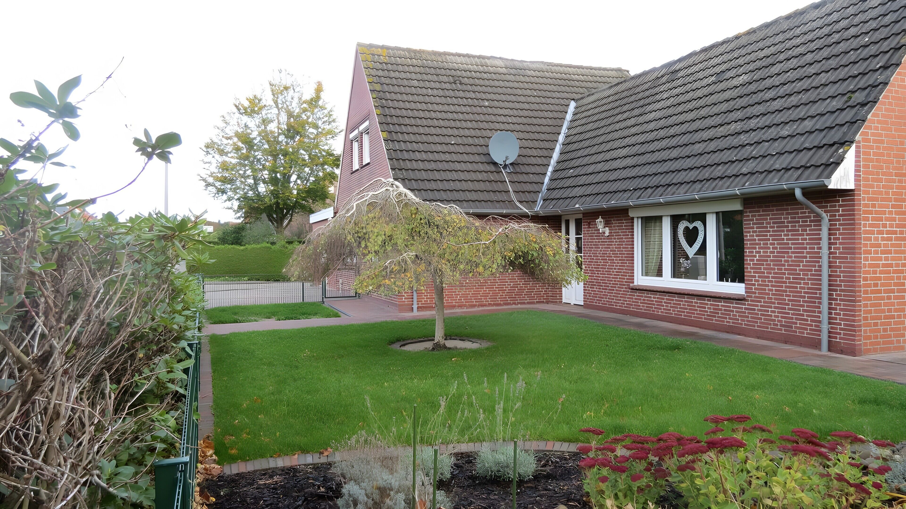Ein Wohnhaus mit Backsteinfassade, geneigtem Dach und einem kleinen Garten mit Rasen und Pflanzen.