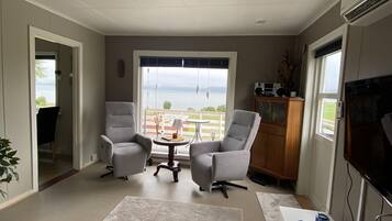 Ein modernes Wohnzimmer mit einem großen Fenster, zwei grauen Sesseln, einem weißen Couchtisch und einem Flachbildfernseher.
