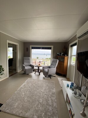 Ein modernes Wohnzimmer mit einem großen Fenster, zwei grauen Sesseln, einem weißen Couchtisch und einem Flachbildfernseher.