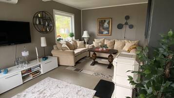 Ein Wohnzimmer mit einer Couch, Fernseher, einer weißen Konsole und einer Zimmerpflanze.