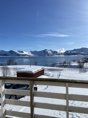 Schneelandschaft mit Bergen im Hintergrund, einem Holzzaun und einem Gebäude mit Schneedecke.