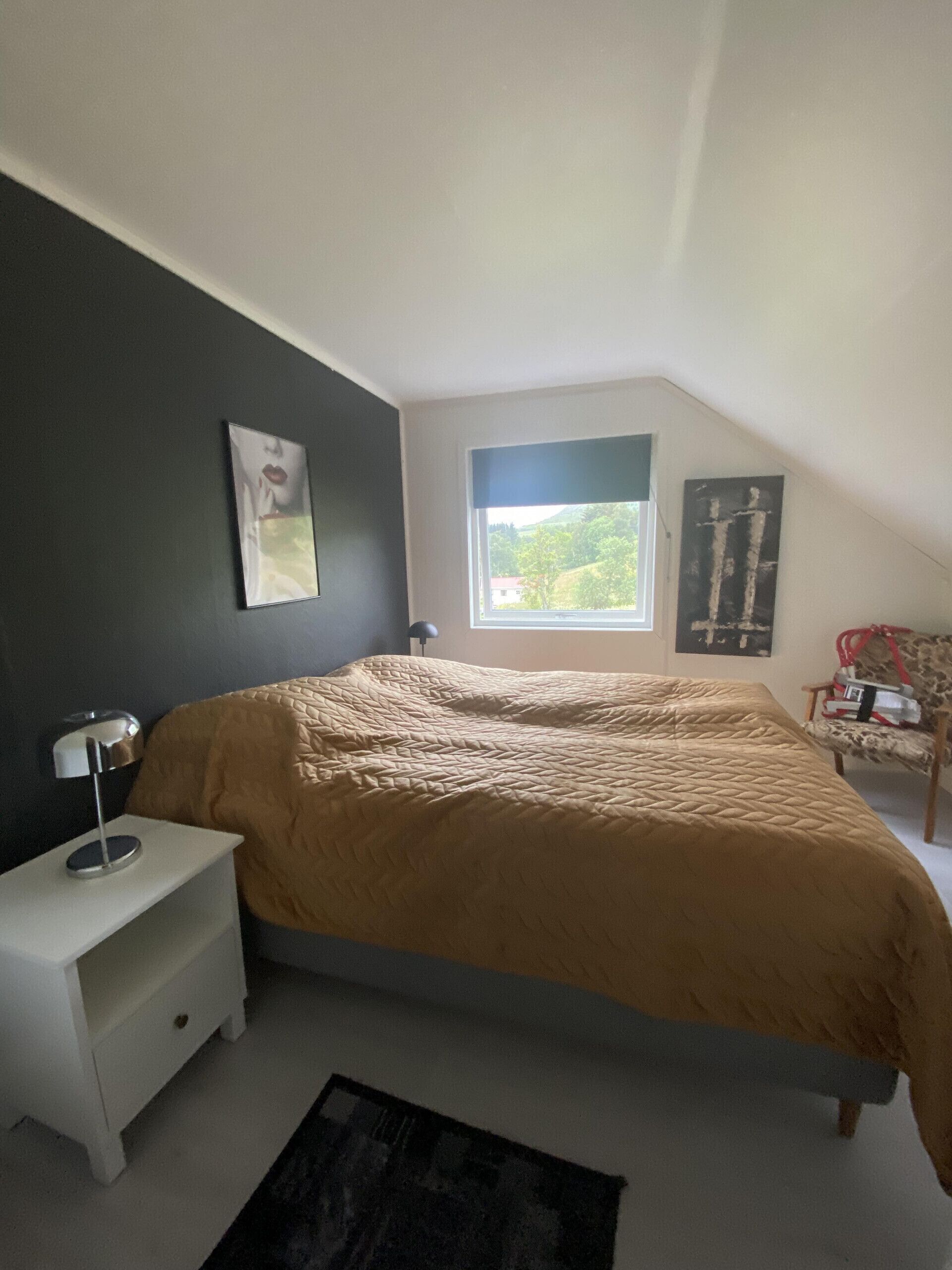 Un dormitorio con una cama, una mesita de noche, una lámpara, una ventana con vistas y una silla.